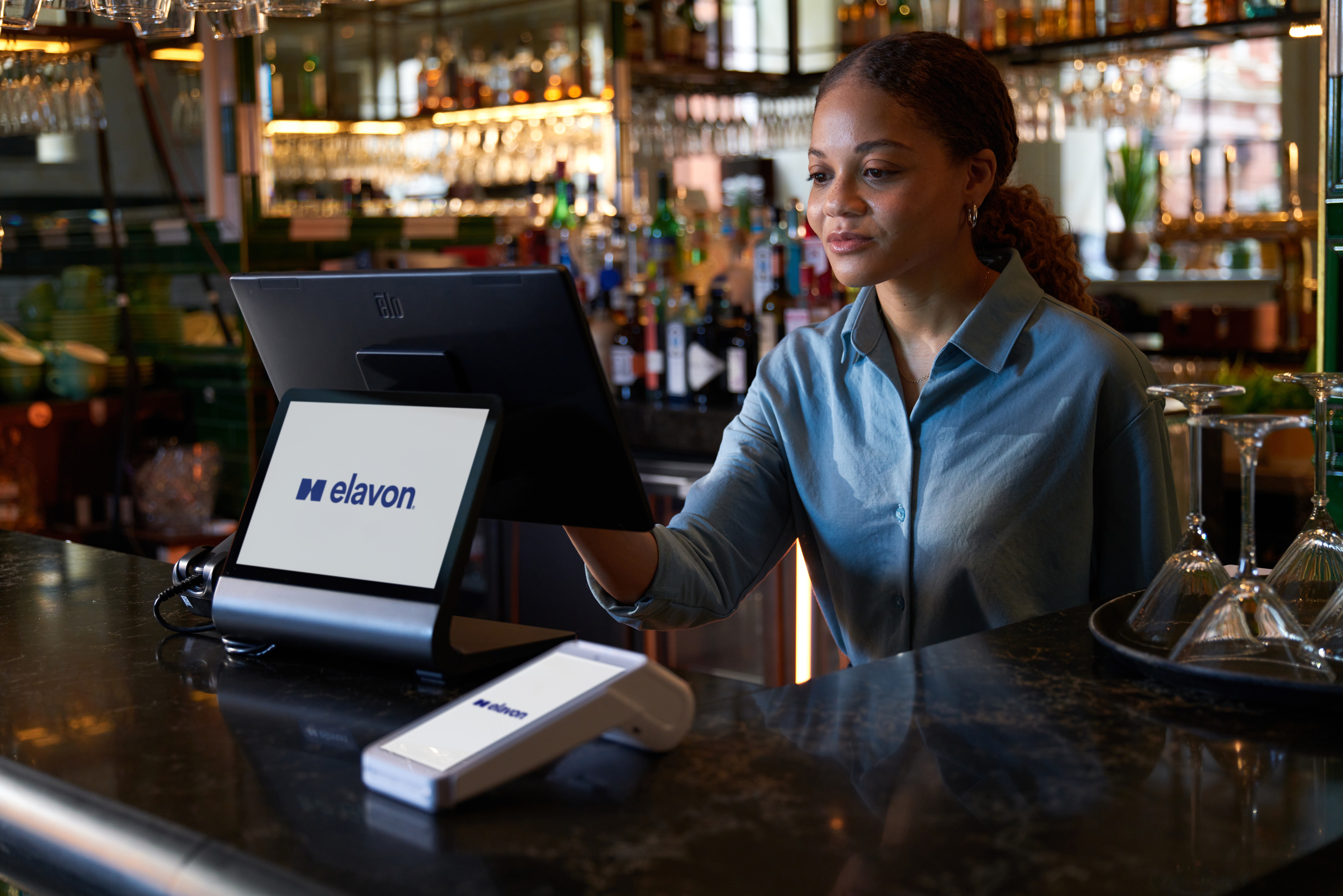 Woman behind the bar using a pos terminal with a DX8000 card machine on top of table