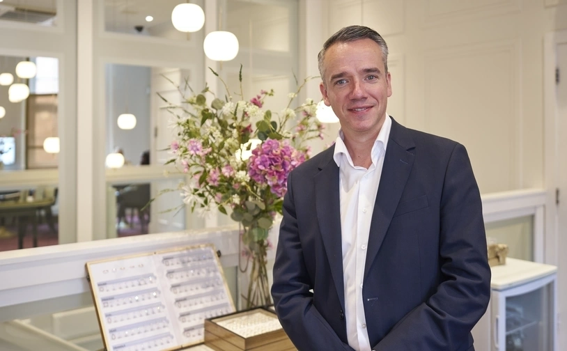  Robert Rock, managing director of Rocks Jewellers, stands in his shop in front of a jewellery display case and a large bouquet of flowers