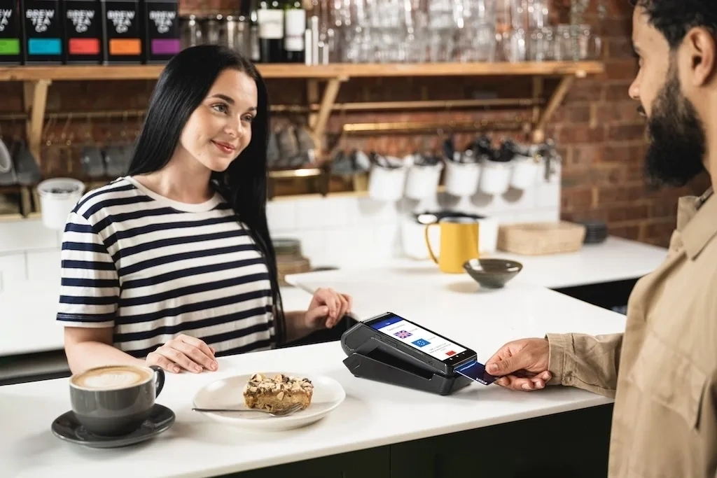 Customer making a card payment at a cafe counter with coffee and pastry on the countertop